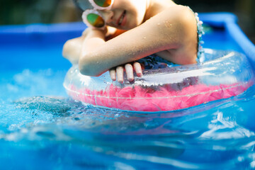 European stylish preteen girl swims on circle in pool at backyard. Funny child in pink glasses with...