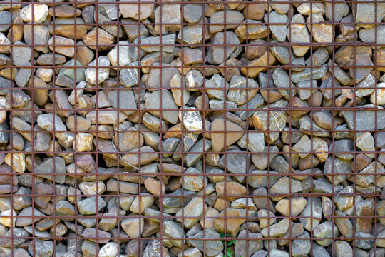 Protection fence or wall made of gabions with gray stones, Old gravel material, Black soil surface with rusty iron cage, Pebble ground pattern, Rock texture, Natural background.