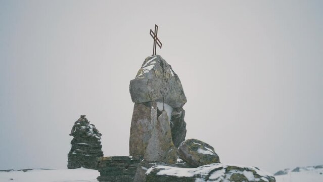 A cross-topped monument surrounded by the stone cairns on the Sognefjellvegen, Norway. Fresh snow on the ground.