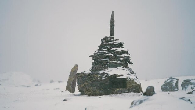 A stone cairn on the Sognefjellvegen in Norway. Fresh snow covers the stone piles. Slow-motion, pan left.