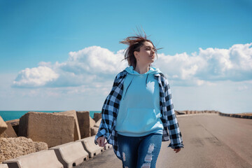 Teenager girl in light blue hoodie and plaid shirt walking outdoor, sunny day and blue sky