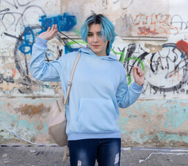 Smiling Blue haired Teenager girl in light blue oversize hoodie against graffiti wall