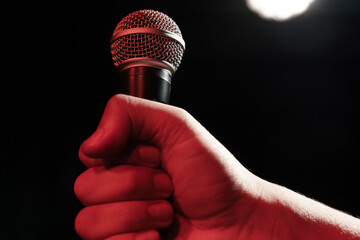 A man's hand holds a professional microphone against the background of stage light