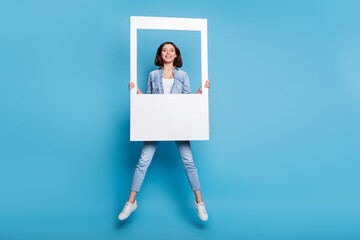 Photo of funny shiny woman wear jeans shirt holding white frame jumping high isolated blue color background