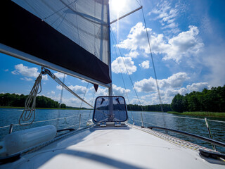 view on a sailing boat bow and sail, sailing on a lake in a sunny summer day - obrazy, fototapety, plakaty