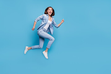 Photo of pretty excited woman wear jeans shirt hurrying jumping high isolated blue color background
