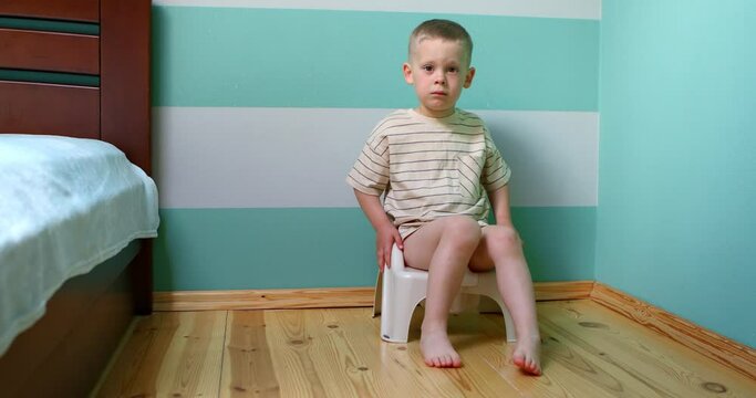 boy on a potty against white wall looking straight to the camera.