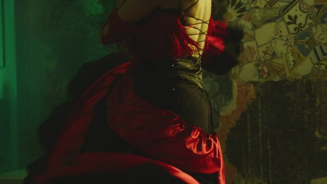 Woman dancing spanish hot dance . Professional dancer in latin dress performs dance movement by skirt . Closeup studio shot of female artist dancing inside dark place . Concept footage of dance art