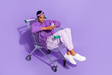 Full length photo of trans bisexual hipster male sit shopping cart surfing in telephone isolated on...