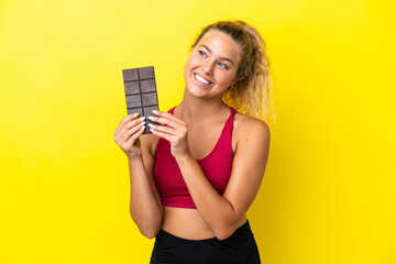 Girl with curly hair isolated on yellow background taking a chocolate tablet and happy