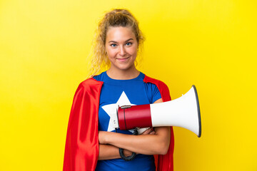 Super Hero woman isolated on yellow background holding a megaphone and smiling