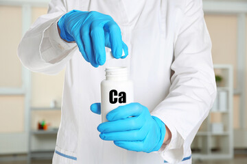 Doctor in medical gloves opening bottle of calcium supplement pills in clinic, closeup