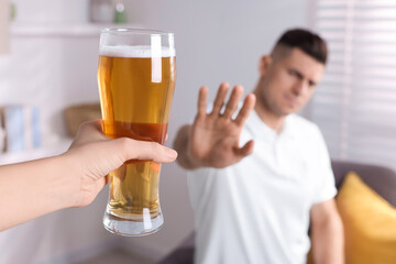Man refusing to drink beer in kitchen, closeup. Alcohol addiction treatment