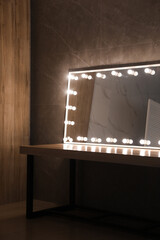 Modern mirror with light bulbs on wooden table in room