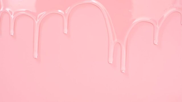 Transparent liquid collagen flowing down on pink background close-up.