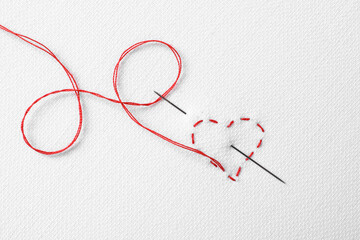 Needle with red thread and stitches in shape of heart on white fabric, top view - obrazy, fototapety, plakaty
