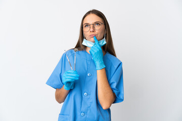 Lithuanian woman dentist holding tools over isolated background having doubts while looking up