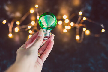 green economy and ideas for the environment, hand showing green light bulb idea with fairy lights bokeh