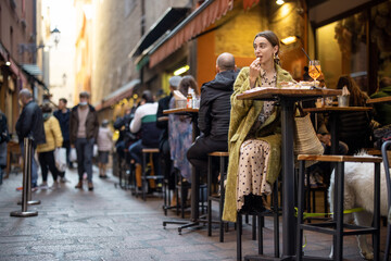 Woman sitting on crowded street at bar or restaurant outdoors in Bologna city. Concept of Italian lifestyle and gastronomy - obrazy, fototapety, plakaty