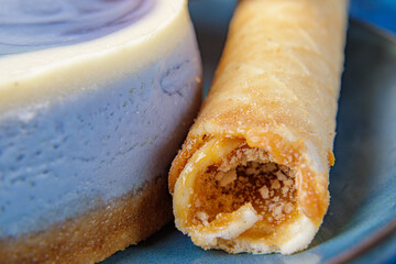 Cheesecake with blueberries and confectionery tubes with condensed milk on a blue plate. Close-up.