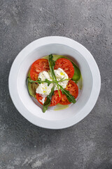 Tomato with ricotta cheese in white plate on grey concrete background