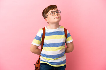 Little redhead caucasian boy isolated on pink background and looking up