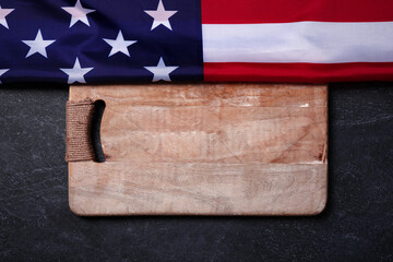 USA flag near empty cutting wood board on dark marble background, concept of american kitchen, layout image
