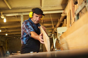 Fototapeta na wymiar Senior carpenter in uniform works on a woodworking machine at the carpentry manufacturing