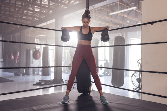 Full length of tired caucasian young female boxer wearing gloves standing at corner in boxing ring