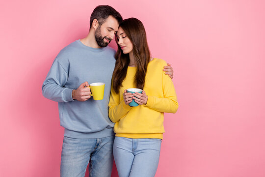 Portrait of two idyllic peaceful partners hug closed eyes hold tea mug isolated on pink color background