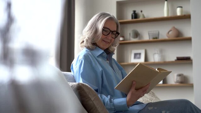 Senior woman sitting on sofa reading book. retirement and senior lifestyle, spending time alone at home.