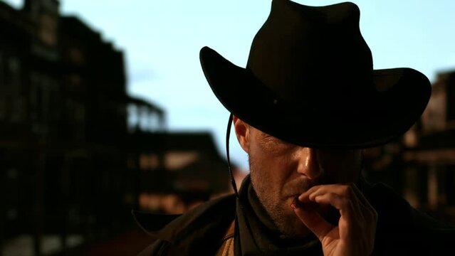 Portrait of cowboy smoking a cigar, old wild west city in the background. Spaghetti, macaroni western style cinematic footage
