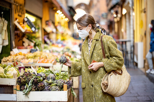 Woman in medical mask choosing fresh products at market stall on the famous gastronomical street in Bologna. Concept of buying local food during pandemic. Idea of Italian lifestyle