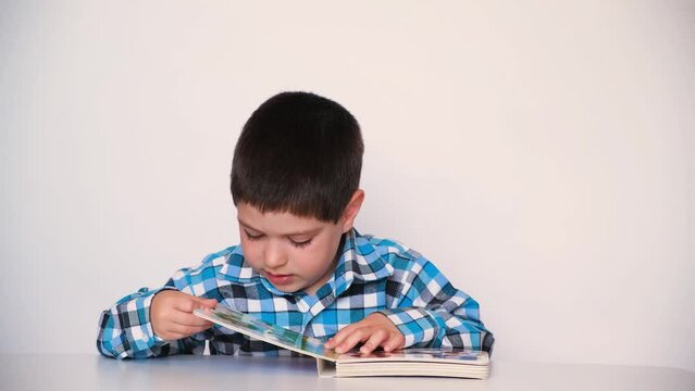 A preschool boy reads a book, closes it and pushes it away from himself.