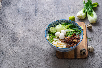 Japanese ramen soup with chicken, egg, chives and bok choy on concrete background.