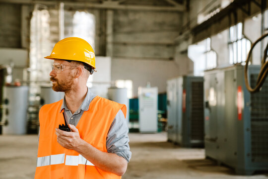 White man wearing helmet using radio set while working at factory