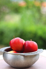 Silver bowl filled with red apples in the garden. Selective focus.
