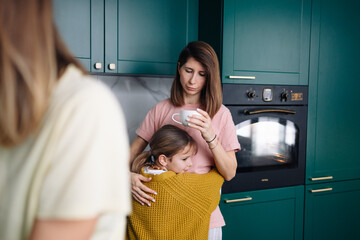 A lesbian family with their daughter is standing in a green kitchen and gently hugging