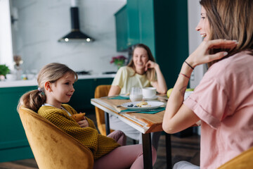 LGBT lesbian family with their daughter sitting at the kitchen table, having breakfast and smiling