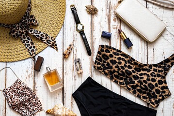 Flat lay view of fashion accessories for beach holiday, travel to covid, face mask, leopard print swimsuit, perfume and straw hat