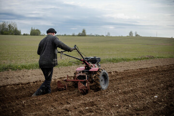 male farmer plows the land with a garden walk-behind tractor. Home farming concept.