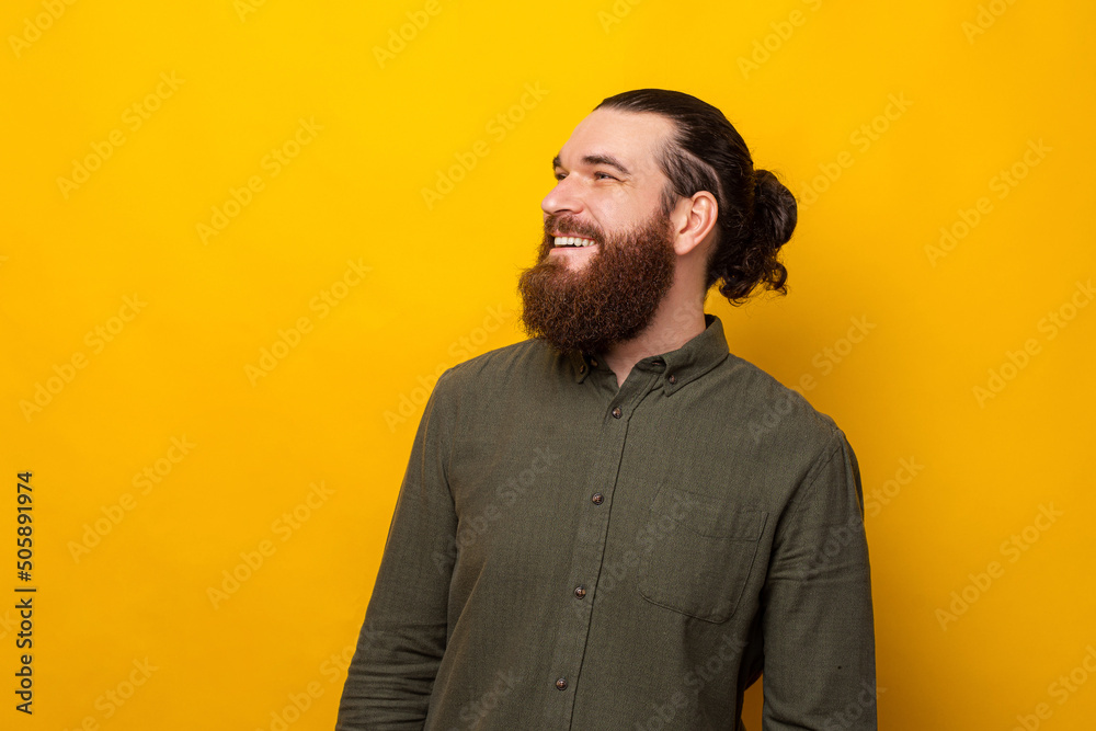 Wall mural Close up portrait of a handsome bearded man smiling and looking aside over yellow background.