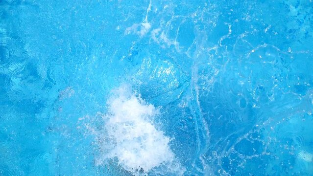 Top view of young woman jumping in pool and splashing crystal clear water. Unrecognizable girl resting and having fun on resort. Lady relaxing during summer vacation or holiday. Slow motion Close up