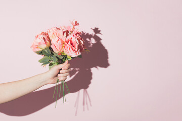 Hand holding flower arrangement against pastel pink background. Minimal modern flower concept.