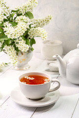 Obraz na płótnie Canvas Useful spring tea with bird cherry in a white cup on a light background