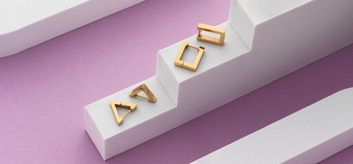 Panorama of Two pairs of golden modern earrings on white and purple geometric background with copy space