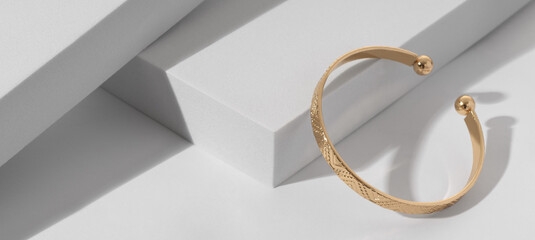 Panoramic shot of a Modern gold bracelet with geometric pattern on minimalistic white background - obrazy, fototapety, plakaty