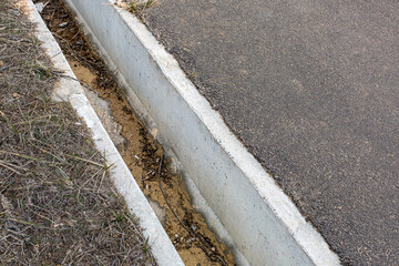 drainage ditch made of concrete on the side of tarmac road contaminated with debris and sand wash...