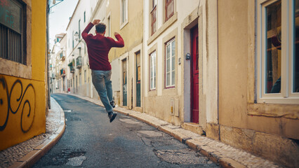 Positive and Happy Young Adult Man in Casual Clothes Actively Dancing while Walking on the Street...