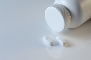 white plastic medicine jar and two white pills. light background